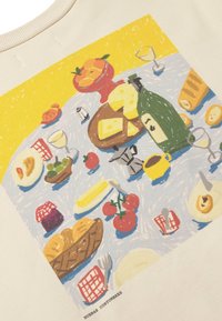 Service de table avec pain, fromage, tomates, bouteille de vin, tasses, fruits et petits pots sur un tissu bleu avec le texte "BUENAS COSTUMBRES" en dessous.