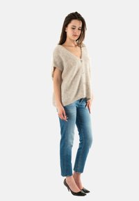 Suéter de punto beige de manga corta con escote en V y tres botones, combinado con jeans azules hasta los tobillos y tacones negros de puntera afilada.