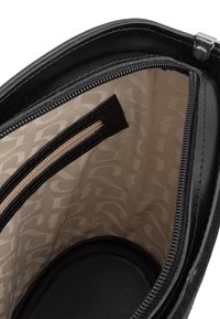 Interno della borsa in pelle nera con tasca con zip. Foderato in tessuto crema con un delicato motivo logo. Texture liscia e forma curva.
