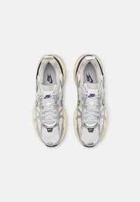 Paire de chaussures de course Nike blanches et argentées avec semelles beiges, vues de dessus sur un fond uni gris clair.