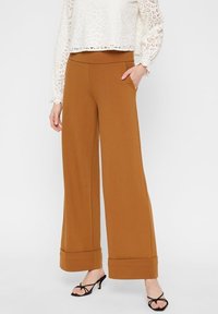 Pantalons à jambe large dans une teinte brun chaud. Fabriqués en tissu doux avec une texture lisse. Dotés d'une taille haute et de bas de jambe retroussés.
