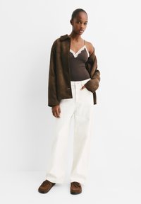 Braune Wildlederjacke aus Kunstleder, weiße weite Hose, dunkelbraunes Tanktop mit Spitzenbesatz und braune Mokassins. Einfaches, modernes Design.