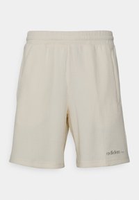 Svetlé béžové sportovní šortky s texturovanou tkaninou, elastickým pasem a jemně vyšitým logem na dolní levé straně.