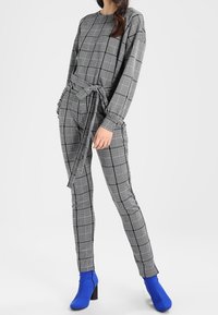 Szara w kratkę koszula z długim rękawem i dopasowane spodnie z wąskim nogawkami, związane w talii. Zestawione z niebieskimi botkami za kostkę. Gładka struktura materiału.