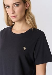 T-shirt nera in cotone con scollo rotondo e maniche corte. Presenta un piccolo logo ricamato in oro sul lato sinistro del petto.