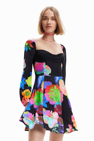 Abito nero floreale con grandi motivi floreali colorati. Maniche lunghe a sbuffo con polsini elasticizzati. Corpino aderente e gonna svasata.