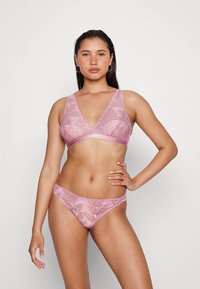 Soutien em renda e bikini combinando em rosa claro. Padrão floral com material transparente. O soutien tem decote em V e não tem aro.