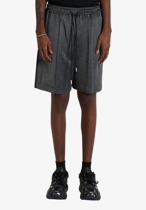 Persona che indossa pantaloncini larghi grigio scuro con coulisse, calzini neri alla caviglia e sneakers nere chunky, in piedi con le mani rilassate lungo i fianchi.