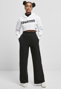 Hoodie corto bianco con logo "STARTER", abbinato a pantaloni della tuta neri larghi. Tessuto strutturato, vita elastica, vestibilità regolare.