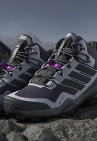 Pari mustavalkoisia ja violetteja Adidas Terrex -vaelluskengät Gore-Texillä lepäilemässä kivikkoisella maastolla ulkona.