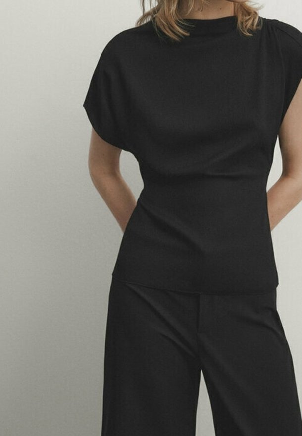 Schwarzes Top mit kurzen Ärmeln, hohem Kragen und lockerem Schnitt. Hergestellt aus einem glatten, strukturierten Stoff mit minimalen Nähten und klaren Linien.