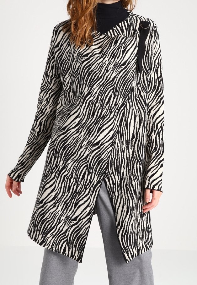 Tunic med zebra-mönster i krämfärgad och svart stickning, med en draperad design, asymmetrisk fåll och en detalj med sidoförbånd.