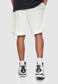 Hvide mesh shorts med en kontrasterende lysfarvet manchet, parret med sorte og hvide sneakers. Synlig tekstureret stof og sporty design.