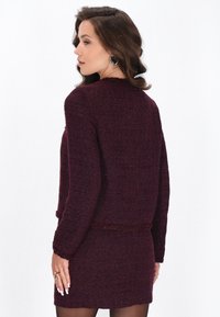 Burgundi tweed kast, mille tekstuuriga viimistluse ja säbrulise äärisega, millel on pikad varrukad ja sobiv lõige. Tagantvaates on lihtne kaelus.