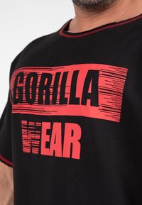 Black t-shirt with red text reading "GORILLA" and "WEAR." Features contrasting red stitching at the neckline. Displayed on a neutral background.
