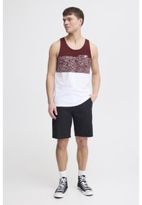 Männliches Tanktop in Weinrot und Weiß, ausgestattet mit einem strukturierten Paneel, kombiniert mit schwarzen Shorts und High-Top-Sneakern. Einfaches Design ohne Grafiken.