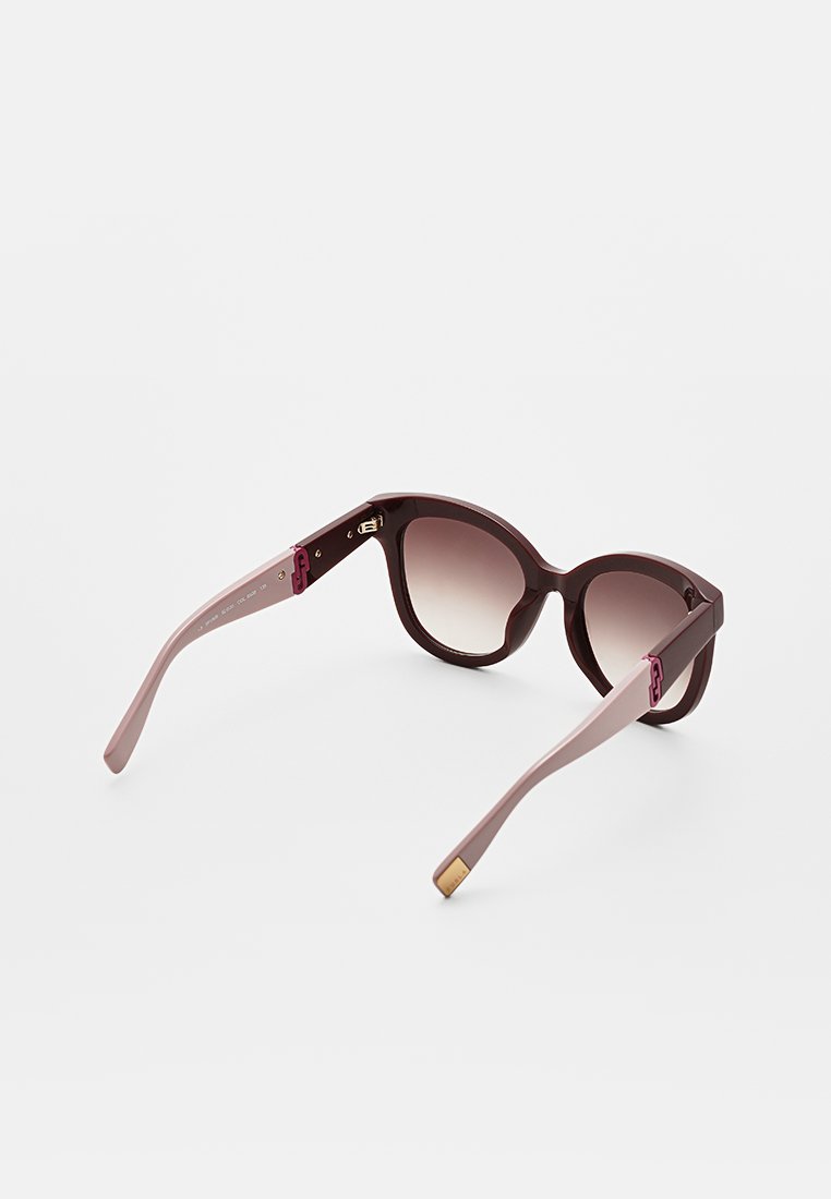 Lunettes de soleil surdimensionnées avec des verres dégradés allant de prune foncé à marron clair, dotées d'une monture bourgogne brillante et de branches roses avec des accents dorés.