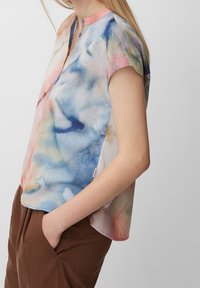 Kortærmet bluse i flerfarvet tie-dye design med nuancer af blå, pink og grøn. Har en rund halsudskæring med knapper. Blødt stof.