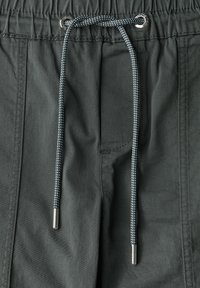 Mörkgröna byxor med elastiskt midjeband och dragsko. Har silverfärgad ögla och texturerad tyg. Avslappnad design.