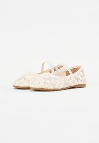 Scarpe basse con tomaia in rete crema caratterizzata da un motivo floreale ricamato. Cinghie elastiche sul collo del piede e una suola morbida di colore marrone.