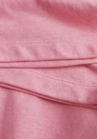 Rožnata tkanina z rebrasto teksturo, ki ima spojene šive in nekoliko obešeno zasnovo, kar prikazuje gladko, enakomerno šivanje.