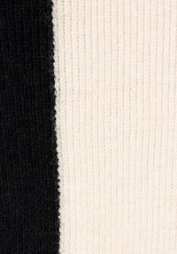 Gebreide stof met een contrast van zwarte en crèmekleurige delen, met een geribbelde textuur en zachte vezels die overal zichtbaar zijn.