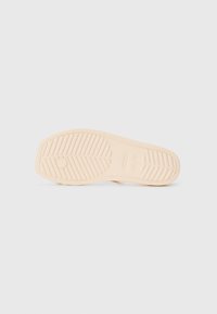 Beige rubber sneaker sole with a textured, ribbed pattern, featuring a circular logo detail and sturdy design.
