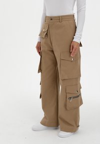 Khaki cargo broek met meerdere zijzakken, ritssluiting en drukknoopsluitingen. Gemaakt van een stevig materiaal met een relaxte pasvorm.