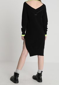 Svart stickad klänning med V-ringning och detalj på ryggen. Långa ärmar med neongröna kantar och sidoslit. Matchad med svarta ankelstövlar.