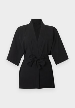 Μαύρο σακάκι στυλ κιμονό με μανίκια μέχρι τον αγώνα και φιόγκο στη μέση, σε ανοιχτό φόντο.