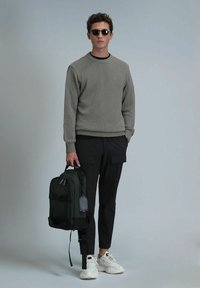 Grijze, gestructureerde trui, donkere broek, witte sneakers en een groene rugzak met zwarte banden. De rugzak heeft een label aan de zijkant.
