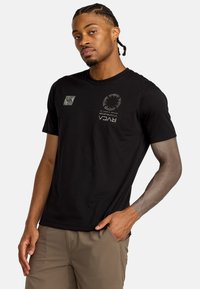 T-shirt nera a maniche corte con grafiche stampate sul davanti, inclusi un logo e disegni circolari, con colletto girocollo e vestibilità comoda.