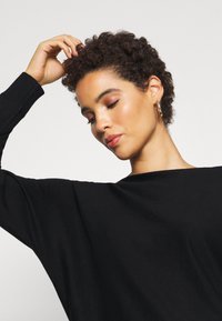 Zwarte, oversized trui met brede mouwen en een zachte textuur. De halslijn is bootvormig, wat zorgt voor een vloeiende silhouet.
