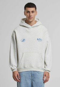 Hanorac cu glugă de culoare gri deschis, cu un buzunar frontal, având text albastru "A.C.L." și un grafic, fabricat dintr-un material moale. Croială relaxată.