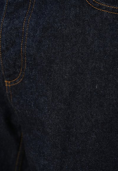 Tamno plavo traper platno s glatkom teksturom i vidljivim uzorkom tkanja, naglašeno narančastim šavovima duž šavova i džepova.