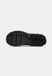 Suola di scarpa sportiva nera, con un motivo di battistrada robusto, materiale in gomma testurizzata e scanalature distinte per aderenza e stabilità.