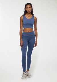 Niebieski stanik sportowy i legginsy o wysokim stanie wykonane z gładkiego materiału. Zestaw cechuje się dopasowanym krojem, bezszwową strukturą i brakiem widocznych wzorów.