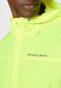 Helle gelbe leichte Jacke mit Kapuze, ausgestattet mit grauem "ENDURA"-Logo, Frontreißverschluss und Schlaufen am Kragen zur Anpassung.