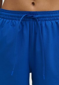 Pantalones cortos azul brillante con cintura elástica y cordón. Textura de tela suave; presenta una costura cosida a lo largo del costado.