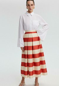 White blouse with a collar and bell sleeves, paired with a long skirt featuring bold red and cream horizontal stripes.