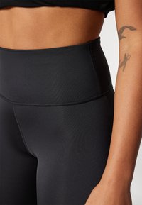 Leggings neri a vita alta in tessuto elasticizzato, con una texture liscia e cuciture piatte per il massimo comfort. Senza motivi visibili o accessori.