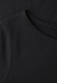 Gros plan sur un t-shirt noir à col rond montrant une couture fine et une texture de tissu en coton lisse.