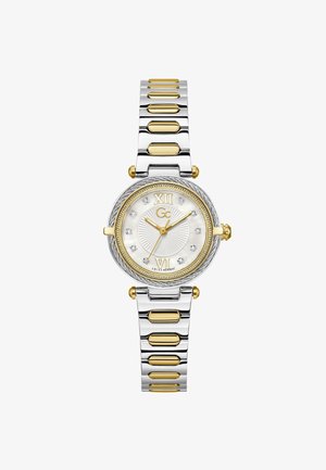 Sølv- og guldfarvet metalur med en rund hvid perlemorsskive, romertal og krystaldetaljer på et sammenkædet armbånd.