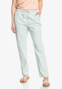 Pantalones de algodón verde menta claro con cintura elástica y cordón, con un corte relajado. Combinados con sandalias blancas de tiras.