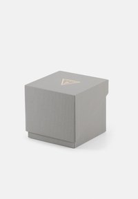 Boîte d'emballage rectangulaire grise avec une surface texturée et un design angulaire. Présente un logo triangulaire doré sur le couvercle.
