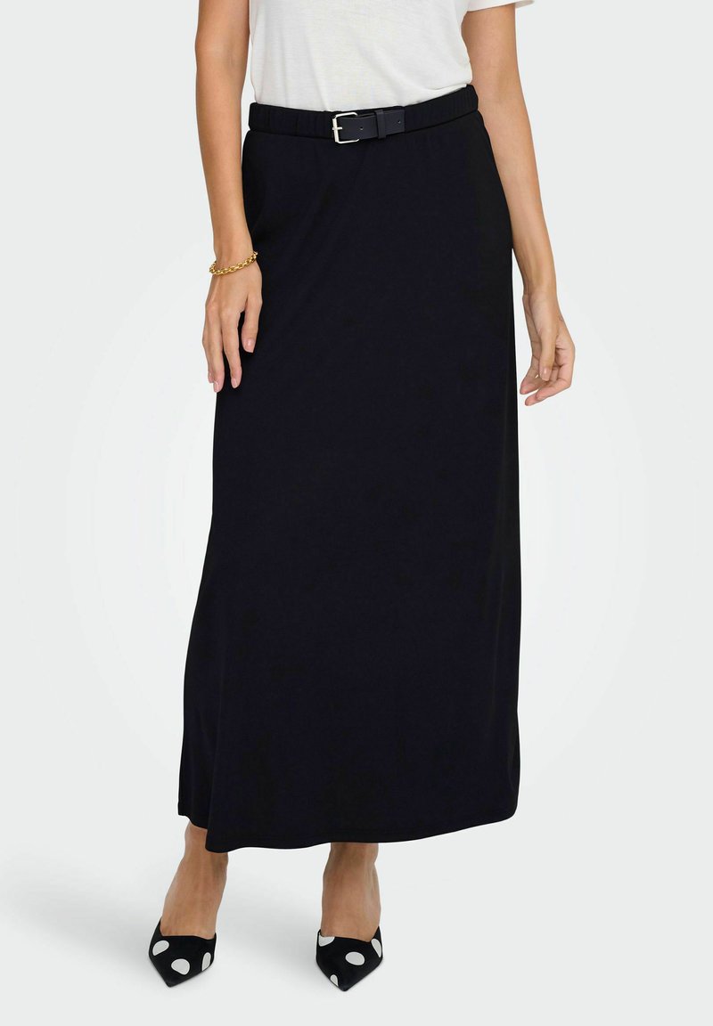 Jupe noire longueur genou en matériau doux, dotée d'une taille ajustée avec une ceinture. Associée à des escarpins à pois noirs et blancs.