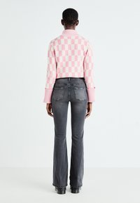 Suéter a cuadros en tonos rosa y crema con puños acanalados, combinado con jeans de campana en gris oscuro. El suéter tiene un cuello alto y un diseño de punto texturizado.