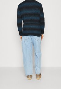 Pullover a maglia a righe blu scuro, vestibilità comoda, con maniche lunghe; abbinato a jeans larghi di un blu chiaro e calzature beige.
