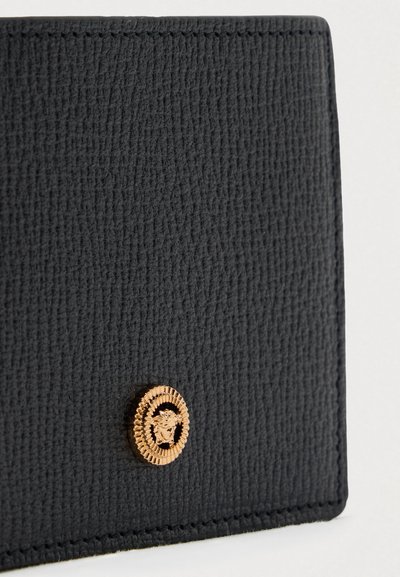 Μαύρο πορτοφόλι από υφαντό δέρμα, με στρογγυλό κούμπωμα σε χρυσή απόχρωση με έμβλημα λιονταριού και ορατή ραφή κατά μήκος των άκρων.