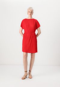 Vestido vermelho plissado com um corte descontraído, mangas curtas e uma cintura elástica. Combinado com sandálias de salto alto bege com tiras.